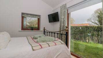 A bedroom with a bed, a window with a view of the garden, and a TV mounted on the wall.