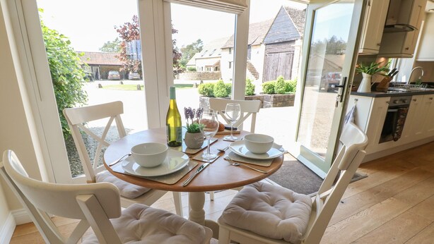 Un coin repas avec une table dressée pour quatre personnes, des chaises blanches et une vue sur l’extérieur.