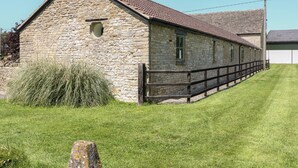 Un bâtiment en pierre avec un toit en tuiles, une clôture en bois et une pelouse devant.