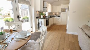 Une cuisine moderne avec des meubles blancs, un coin repas doté d’une table en bois et de chaises blanches, et une vue sur l’extérieur grâce à une porte vitrée.