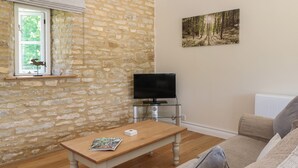 Un salon avec un mur en pierre, une table en bois sur laquelle repose un magazine, un téléviseur posé sur un meuble et un canapé.