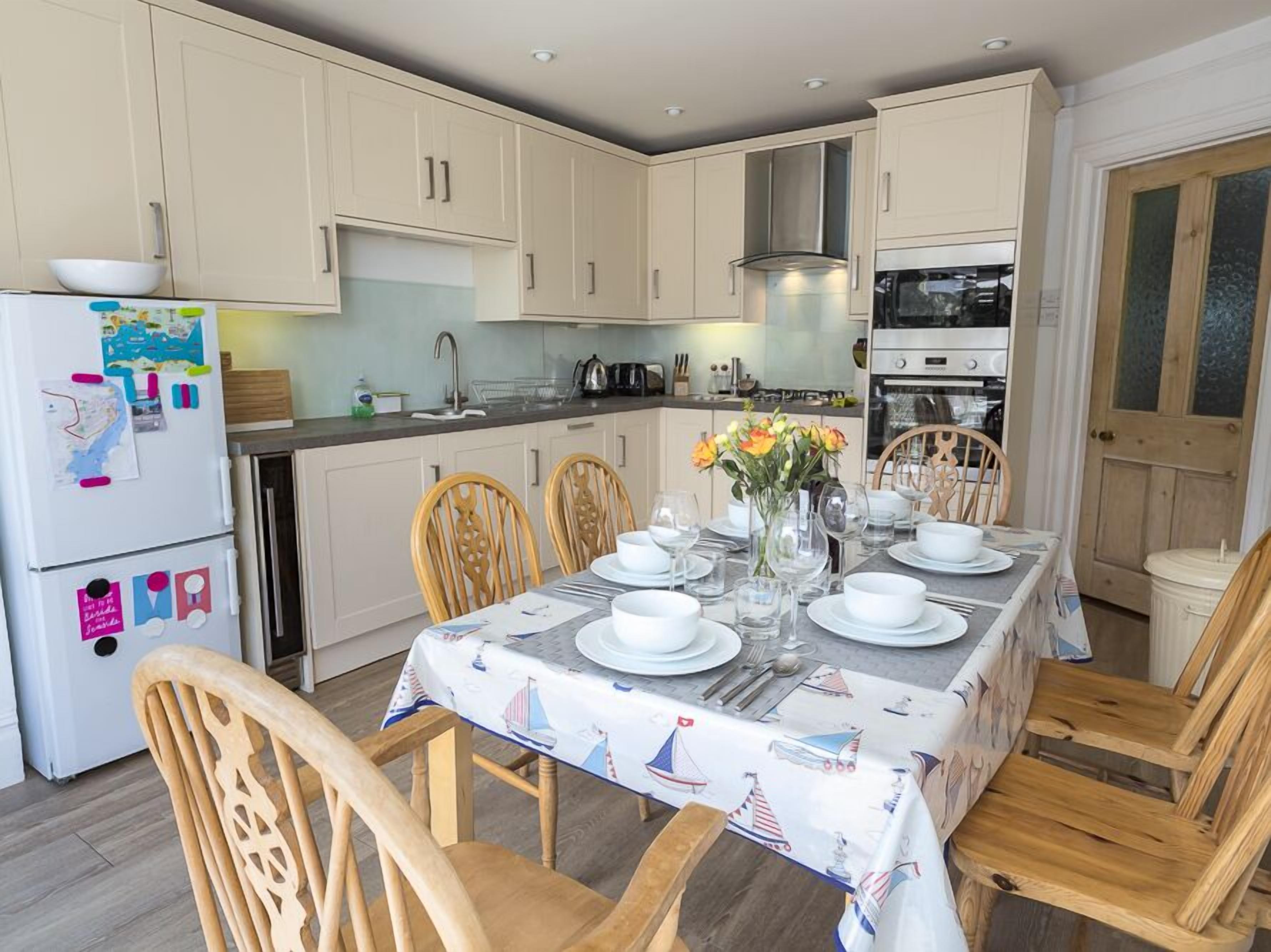 A modern kitchen with white cabinets, a dining table set with white plates and glasses, and a vase with flowers.