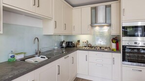 A modern kitchen with white cabinets, a stainless steel range hood, and a built-in oven. - Prospects (Salcombe)