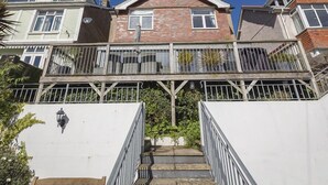 A two-story residential building with a balcony, a staircase leading to the entrance, and a clear blue sky. - Prospects (Salcombe)