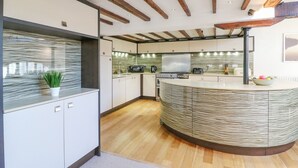 A modern kitchen with a curved island, wooden beams on the ceiling, and a backsplash with a wavy pattern. - Barley Mews (Weymouth)