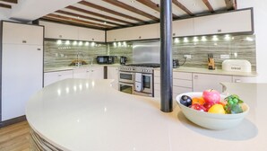 A modern kitchen with a central island, stainless steel appliances, and a bowl of fruit on the counter. - Barley Mews (Weymouth)