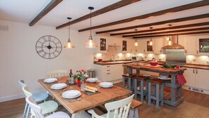 A modern kitchen with wooden beams, pendant lights, and a central island with stools. - Gwyndy Bach (Caernarfon)