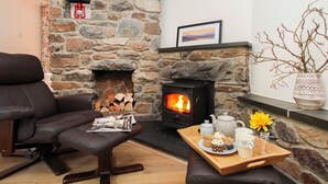 A cozy living room with a stone fireplace, a comfortable leather sofa, a wooden tray with a teapot, cups, and a flower. - Gwyndy Bach (Caernarfon)