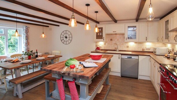 A modern kitchen with wooden beams, a large island, and a red stove. - Gwyndy Bach (Caernarfon)
