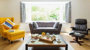 A living room with a sofa, armchair, and chair, a coffee table with a tray of tea and cups, and a window with curtains. - Gwyndy Bach (Caernarfon)