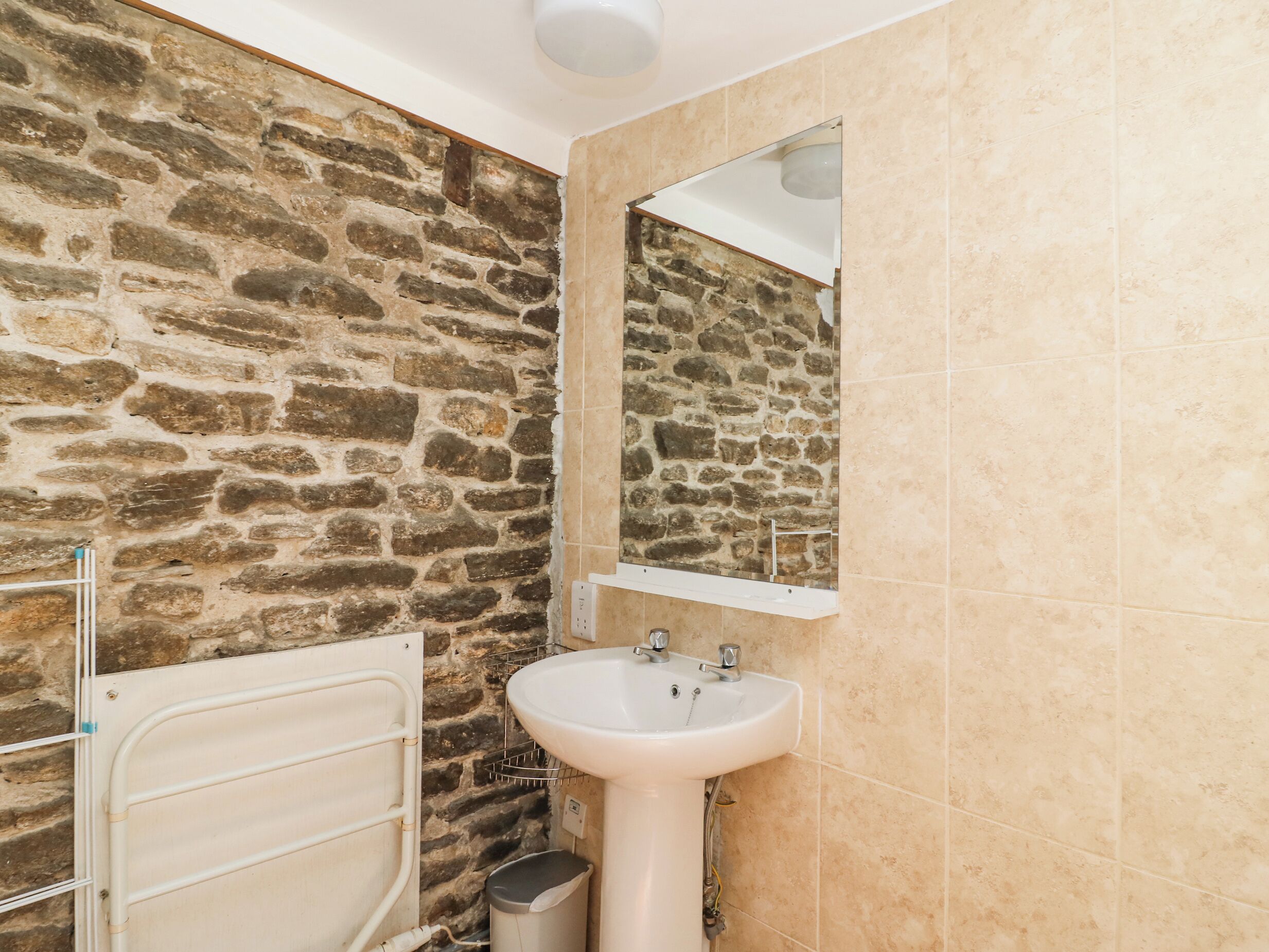A bathroom with a stone wall, a white sink, and a mirror.