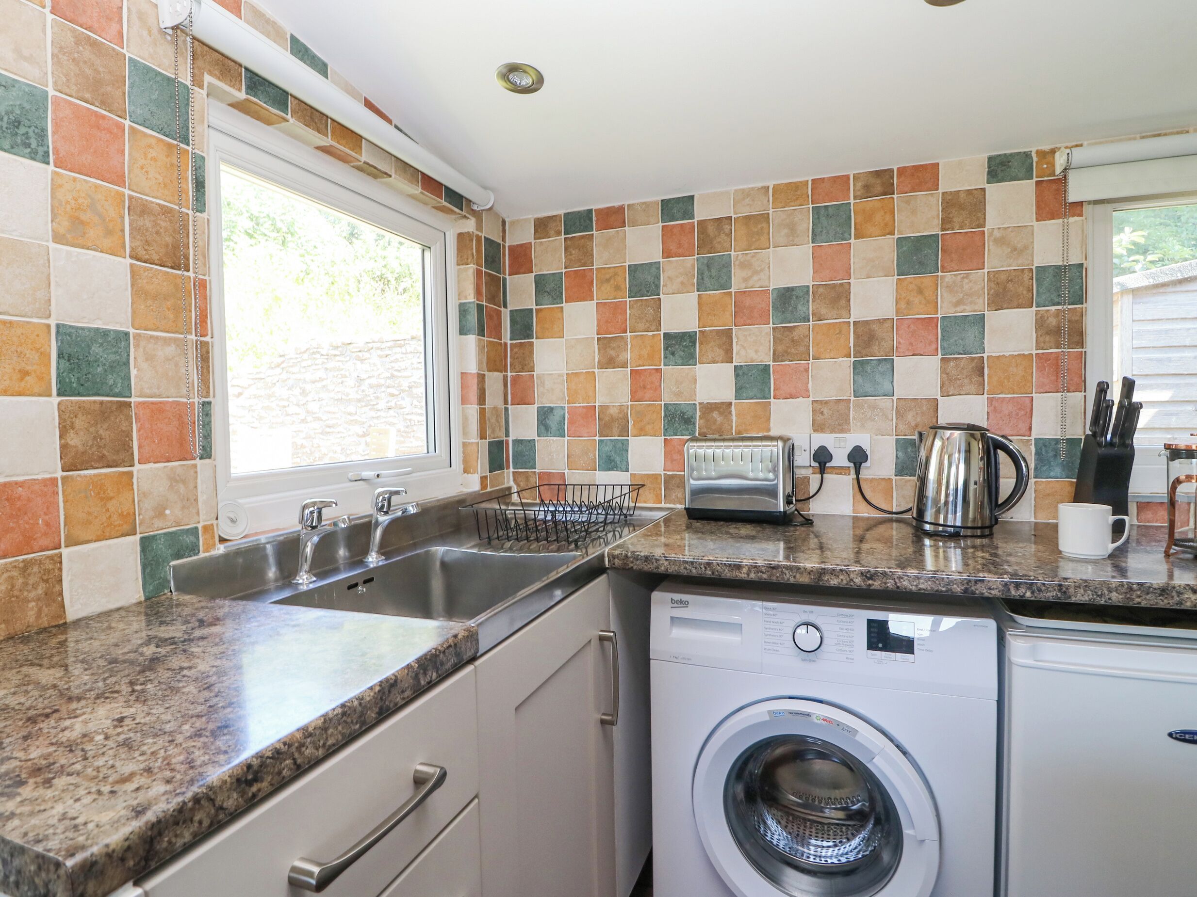 A kitchen with a washing machine, a toaster, and a kettle on the counter.