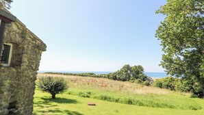 A stone building with a small window, surrounded by a grassy field and trees, overlooking a body of water. - Washingpools (Dorchester)