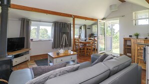 A cozy living room with a sofa, a TV, a dining table with chairs, and a kitchen area visible through an open door. - Washingpools (Dorchester)