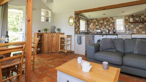 A cozy living room with a grey sofa, wooden dining table, and chairs. A kitchen with a tiled backsplash and wooden cabinets is visible in the background. - Washingpools (Dorchester)