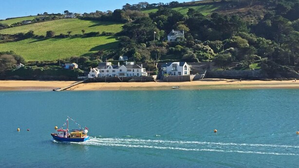 A coastal scene with a boat on the water, a sandy beach, and houses on a hillside. - Seaspray (Kingsbridge)