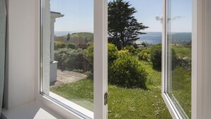 A view from a window with a clear view of a grassy area, a tree, and a distant landscape with hills and the sea. - Seaspray (Kingsbridge)