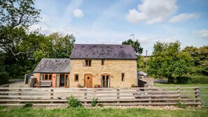 Un bâtiment en pierre de deux étages, doté d’un toit en pente, de portes en bois et d’un petit porche avec un banc.