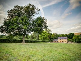 A rural landscape with a large tree and a stone building with a sloped roof.