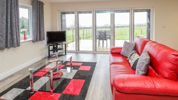 A modern living room with a red leather sofa, a glass coffee table, and a flat-screen TV. - The Donkey Shed (Sherborne)