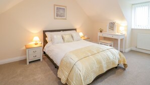 A bedroom with a bed, bedside tables, a desk, and a window. - The Donkey Shed (Sherborne)