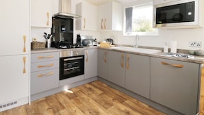 A modern kitchen with grey cabinets, wooden handles, a built-in oven, a stove, and a microwave. - Beech Tree Lodge (York)