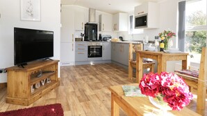 A modern kitchen with a TV, wooden furniture, and a dining area with a table and flowers. - Beech Tree Lodge (York)