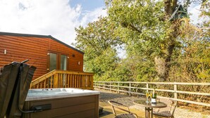 A wooden deck with a hot tub, wicker chairs, and a table with bottles. - Beech Tree Lodge (York)