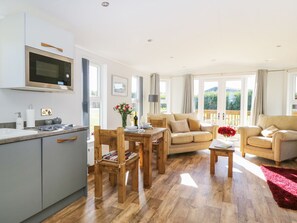A modern kitchen with a built-in oven and microwave, wooden dining table with chairs, a sofa, and a red rug.