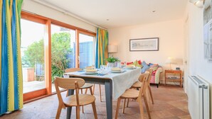 A dining area with a table set for four, wooden chairs, a view through a glass door, and a small side table with a lamp. - Westland (Salcombe)