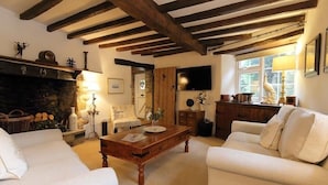 A cozy living room with a fireplace, wooden beams, a television, and comfortable seating. - Pike Cottage (Cheltenham)