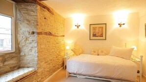 A bedroom with a stone wall, a bed with white bedding, two wall-mounted lights, and a framed picture on the wall. - Pike Cottage (Cheltenham)