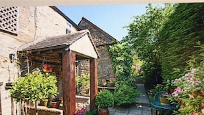 A small garden with a wooden structure, potted plants, and a table. - Pike Cottage (Cheltenham)