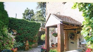 A rustic garden with a wooden pergola, a small shed, and various potted plants. - Pike Cottage (Cheltenham)
