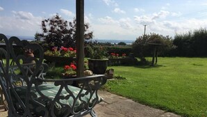 Un patio jardín con un banco de metal, plantas en macetas y vistas al mar.
