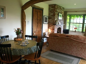 A cozy living room with a fireplace, a dining area with a table set for two, and a patterned sofa. - The Piggery (Lydney)