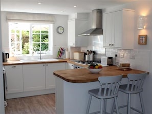 A modern kitchen with white cabinets, a wooden island, and a window with a view of greenery.