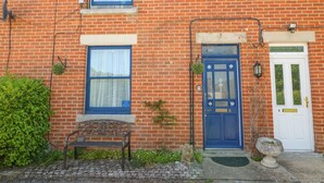 A brick building with a blue door, a bench, and a small garden area. - Studland Cottage (Swanage)