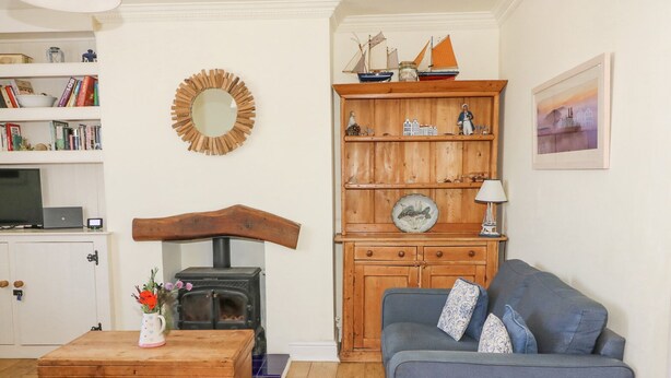 A cozy living room with a fireplace, a blue sofa, wooden furniture, and a bookshelf. - Studland Cottage (Swanage)