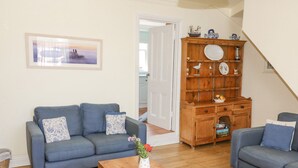 A living room with two blue sofas, a wooden coffee table, and a wooden cabinet with decorative items. - Studland Cottage (Swanage)