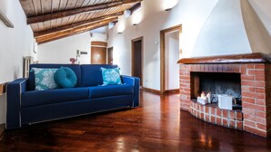 A living room with a blue sofa, a brick fireplace, wooden flooring, and a sloped ceiling. - JOIVY Big Wooden Apartment for 6 near Milano Center (Milan)