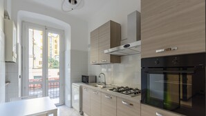 A modern kitchen with a gas stove, oven, and microwave. There is a dining table and chairs, and a view of the outside through a glass door. - JOIVY Monte Suello (Genoa)