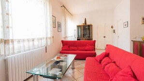 Un saló amb una taula de centre de vidre, dos sofàs vermells, un armari i un radiador.