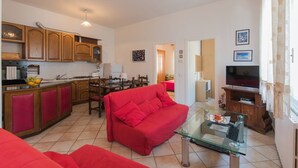 Un saló modern amb un sofà vermell, una taula de centre de vidre i una cuina amb armaris de fusta i una taula de dinar.