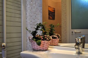 A bathroom with a white sink, a mirror, and two wicker baskets containing plants. - JOIVY Elly's Terrace-old City (Viareggio)