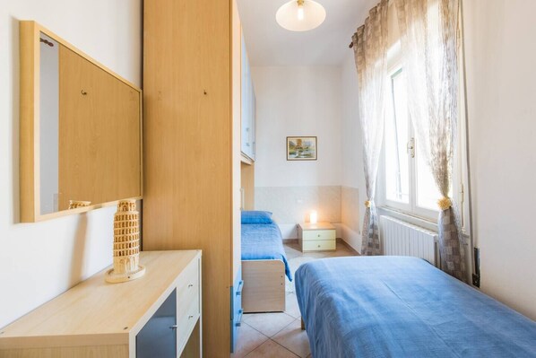 A bedroom with two beds, a wooden dresser, a mirror, and a window with curtains. - JOIVY Elly's Terrace-old City (Viareggio)