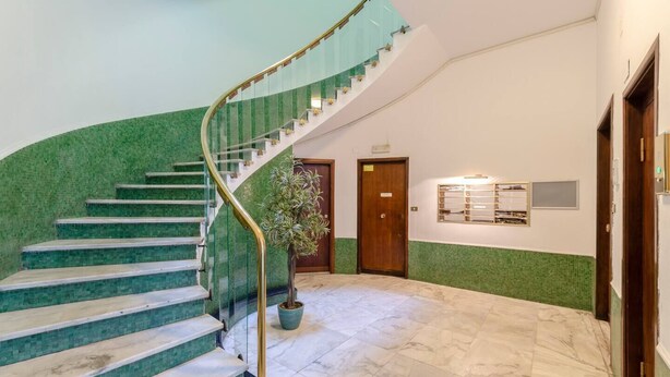 Una escalera curva con paredes de azulejos verdes y suelo de mármol, que conduce a una puerta de madera.