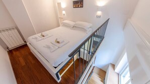 Habitación de hotel con cama, ropa de cama blanca, un cuadro en la pared y vistas al exterior.