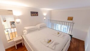 Un dormitorio con una cama grande, una mesita de noche pequeña, una ventana con vistas y una barandilla.