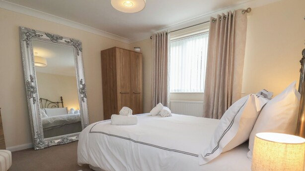 A neatly arranged hotel room with a large bed, a wooden wardrobe, a mirror, and a bedside table with a lamp.